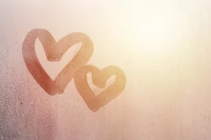 Deux cœurs dessinés sur une vitre embuée, symbolisant l’amour, la douceur et la connexion intérieure, les énergies du mois de février